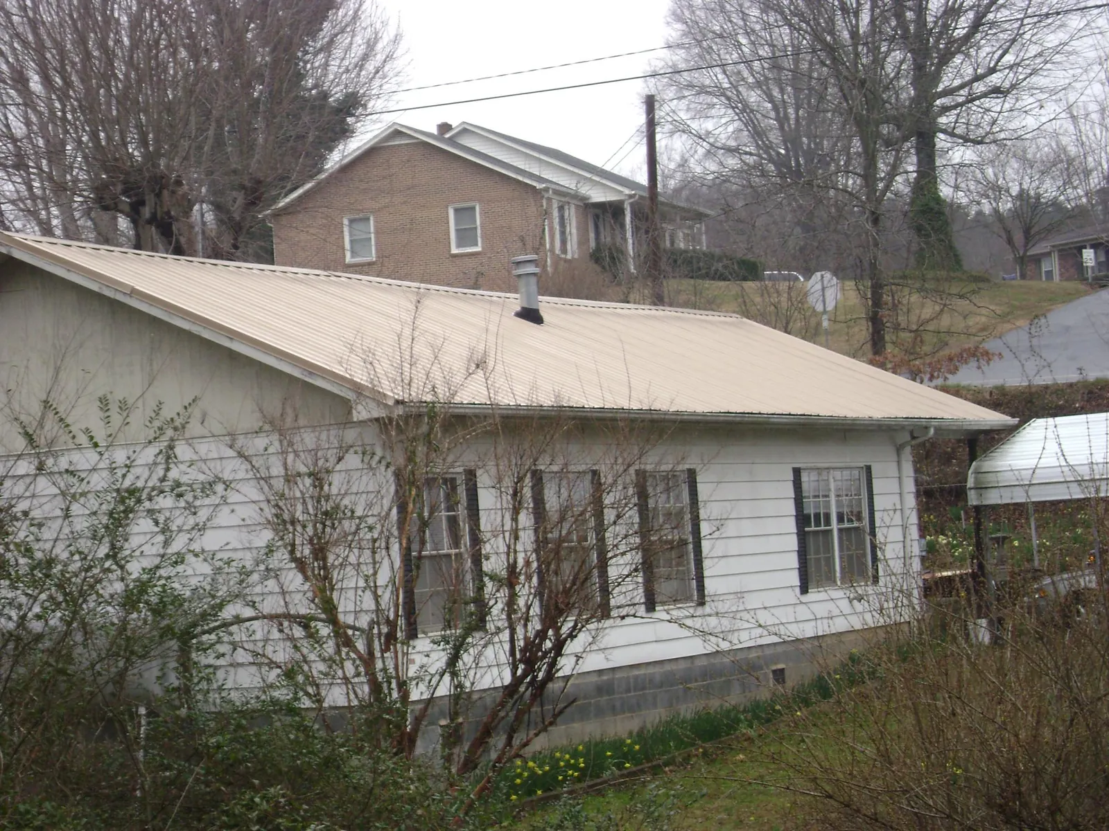 Tan metal roof on a white sided house set into a hillside — Commercial Roofing by Roofing Brothers in Ellsworth