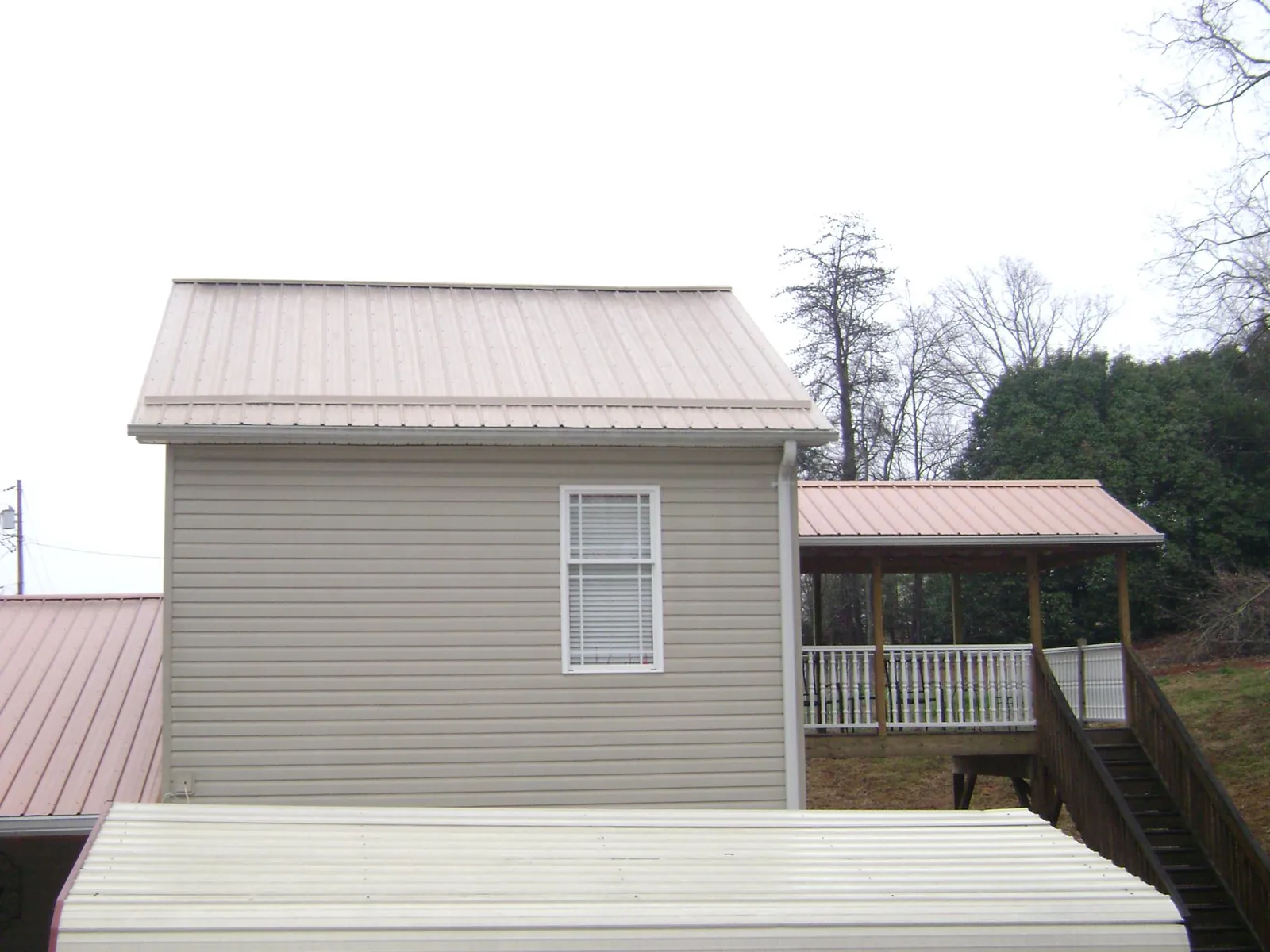 Tan metal roofs on a two story addition and attached porch, from a Roof Replacement job in Ellsworth